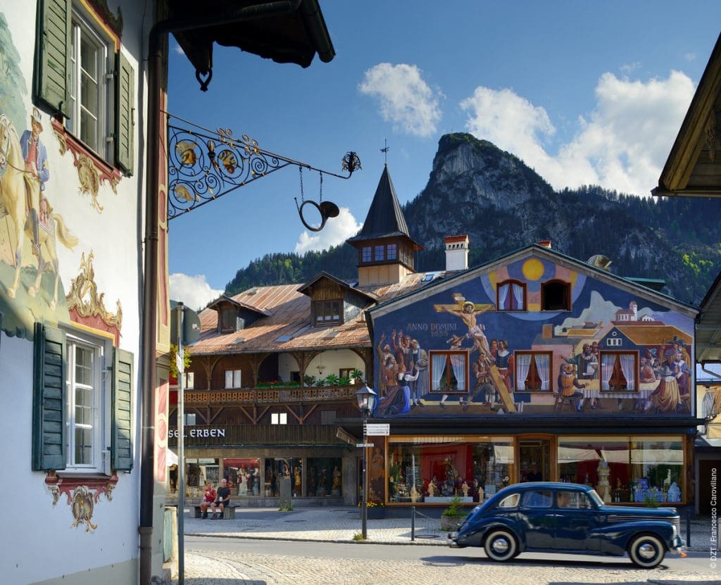 Oberammergau, Bayern, Deutschland - Typical painted façade and architecture in the old town with tourists passing by and the German Alps in the background.