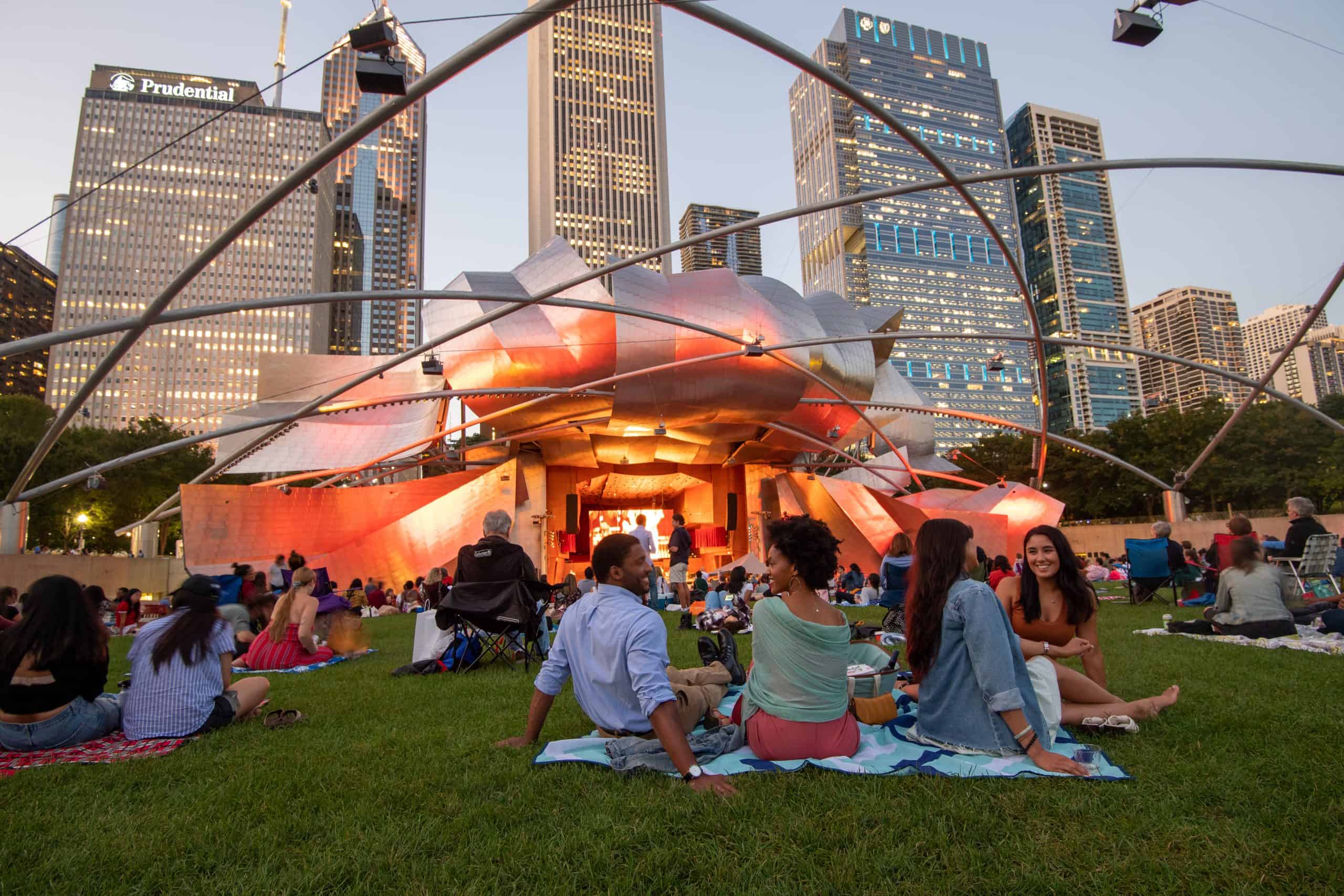 An evening concert draws crowds onto the Great Lawn at Millennium Park, framed by Chicago’s skyline and the glowing Jay Pritzker Pavilion