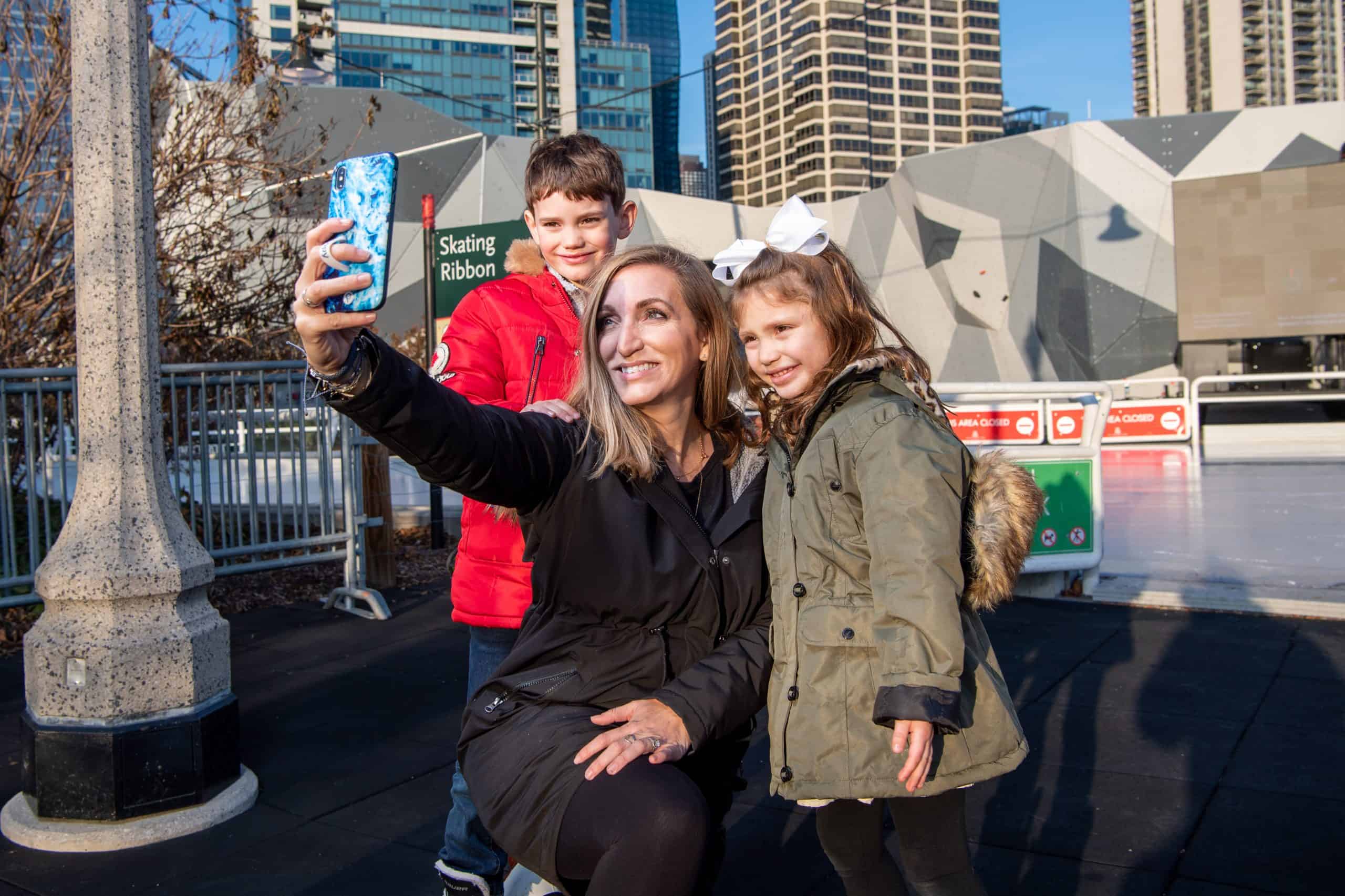 A family pauses for a cheerful winter selfie beside the Skating Ribbon in downtown Chicago