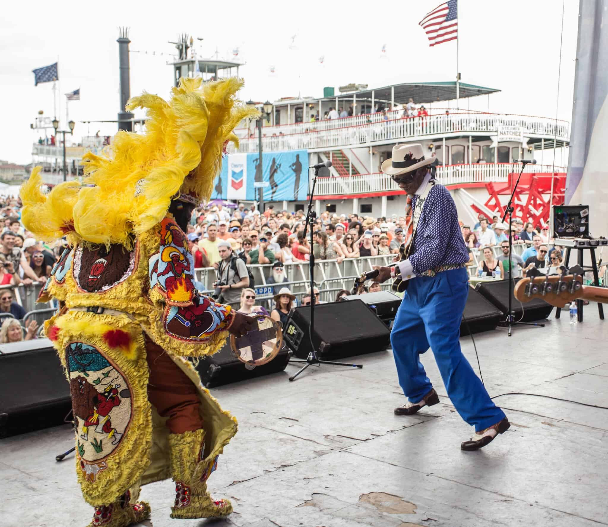 A vibrant Louisiana festival moment with live music, dazzling costume detail and a cheering waterfront crowd