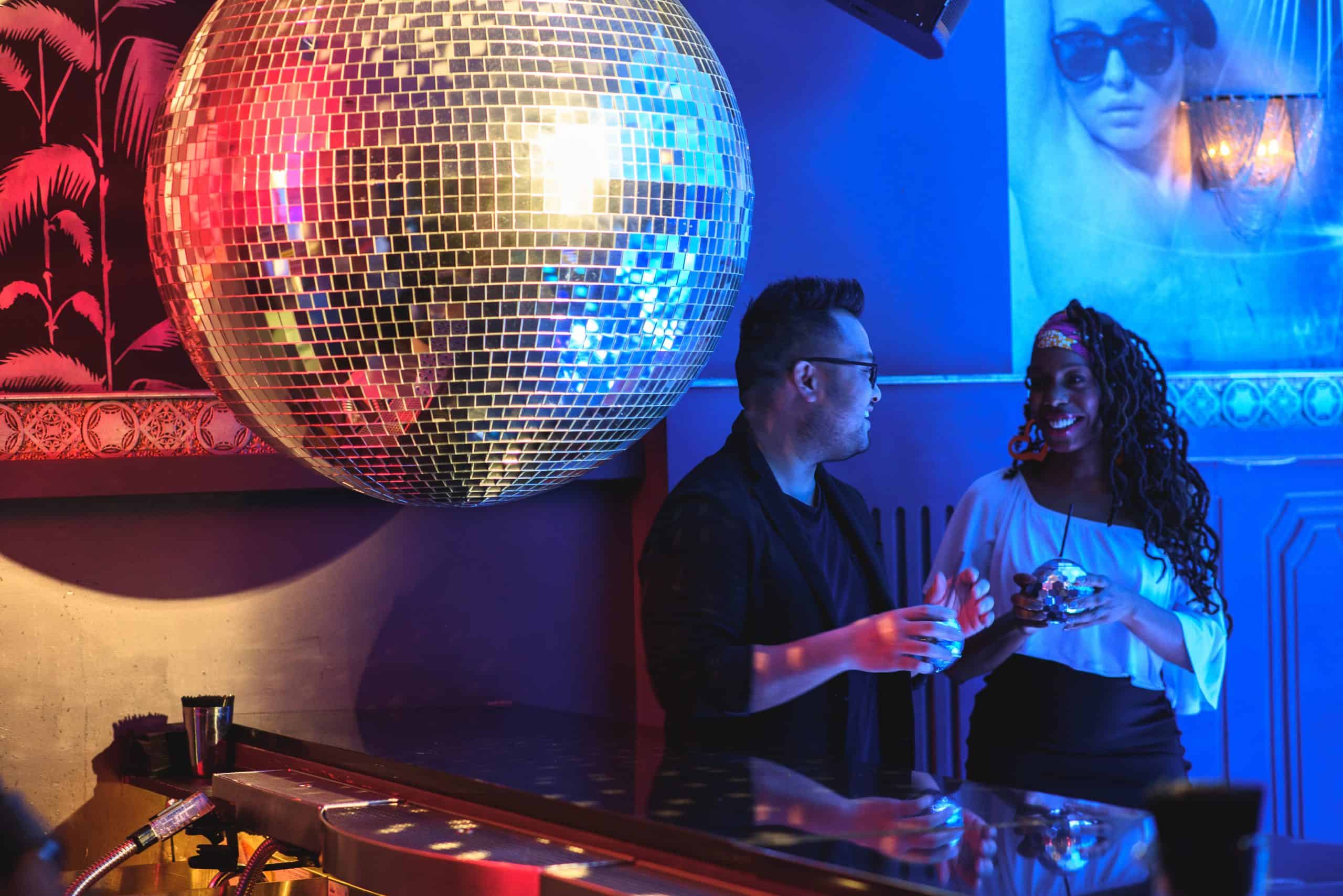 A glittering disco ball sets the mood as nightlife and conversation unfold in a neon washed Chicago lounge