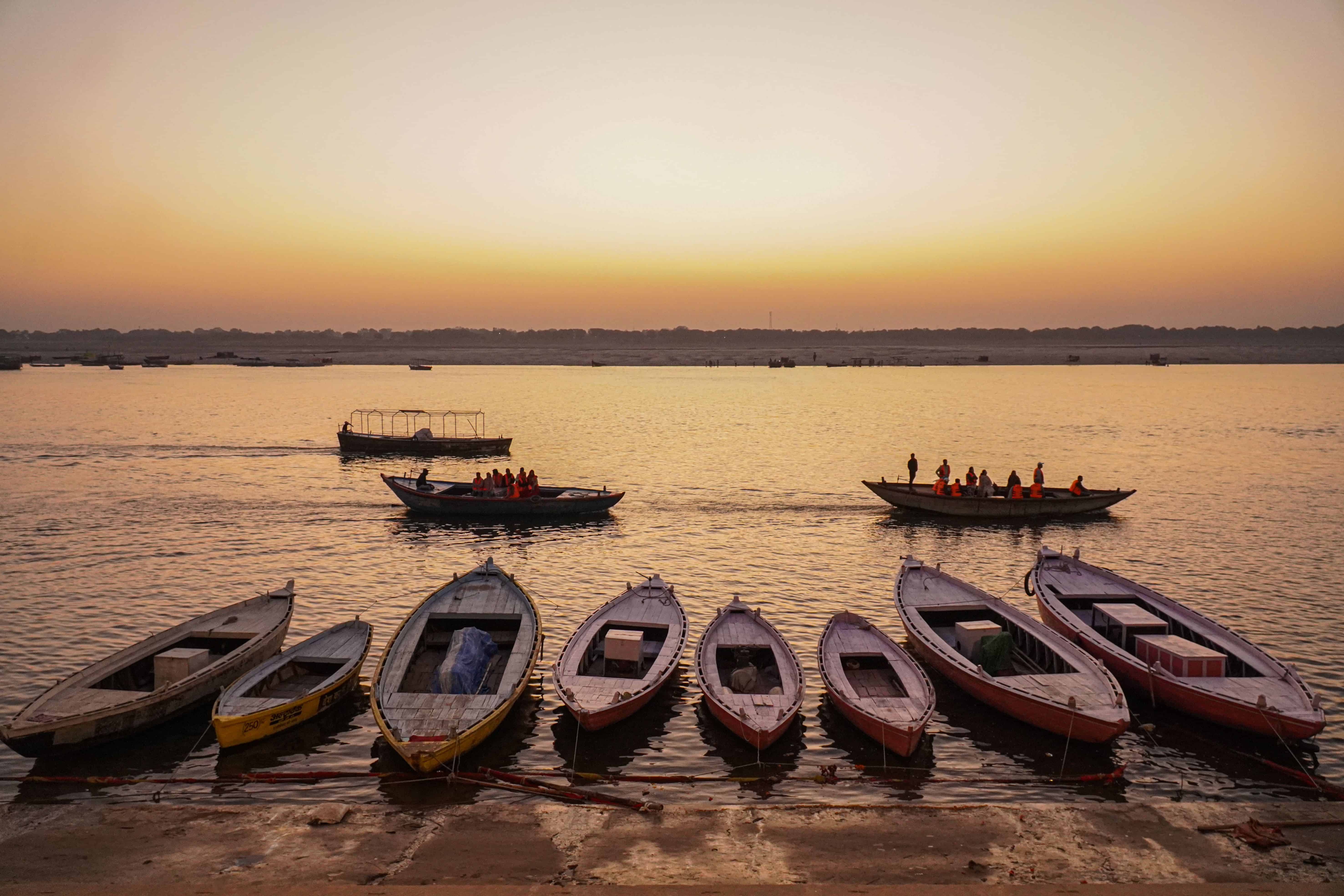 Rowboats peacefully docked with a boat rowed on Ganges River during sunrise in Varanasi. Image Courtesy: Arto Suraj, Pexels