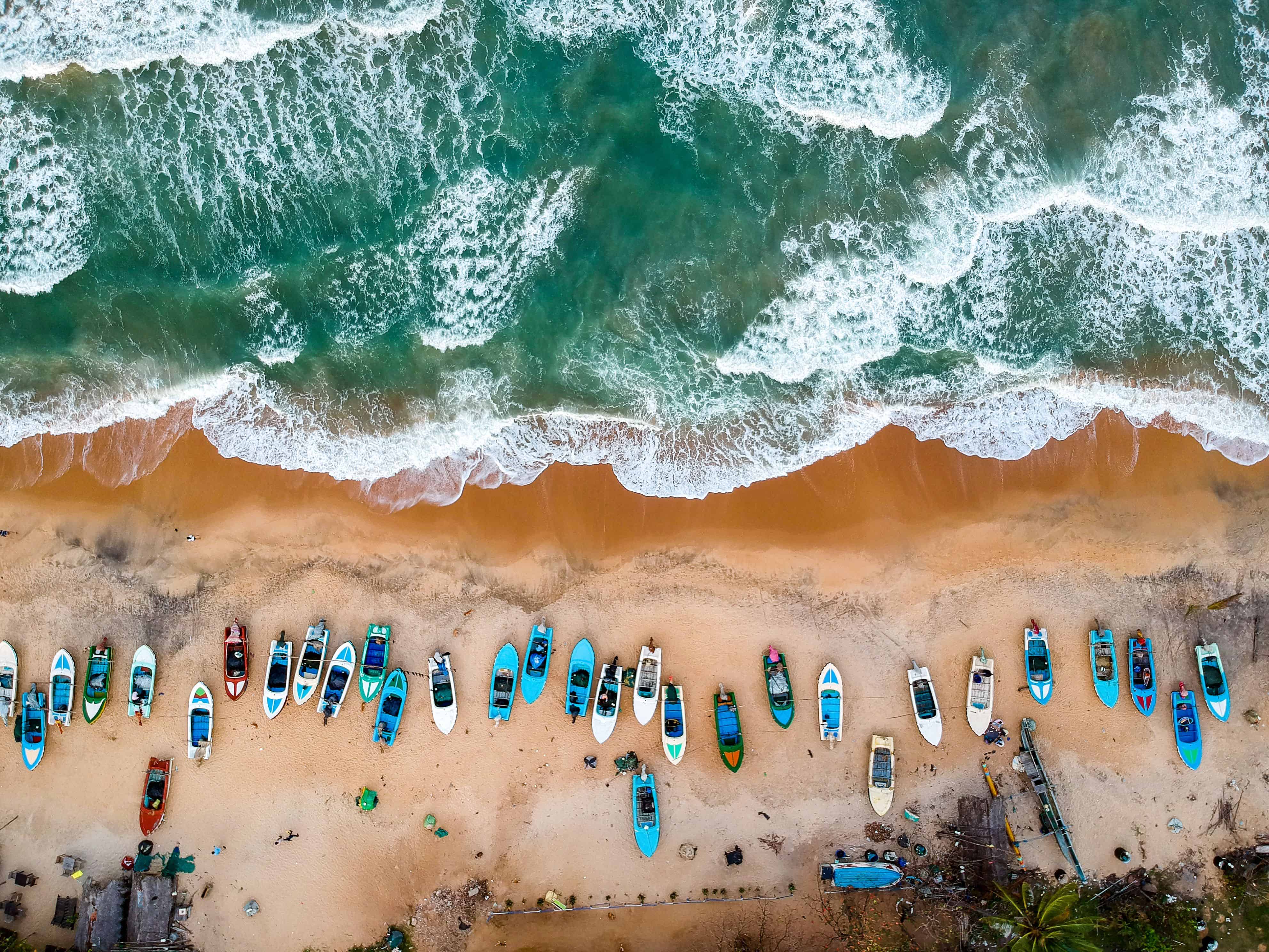 Stunning aerial shot of vibrant boats lined on sandy shores of Arugam Bay, Sri Lanka. Image Courtesy: Pexels, Tomas Malik